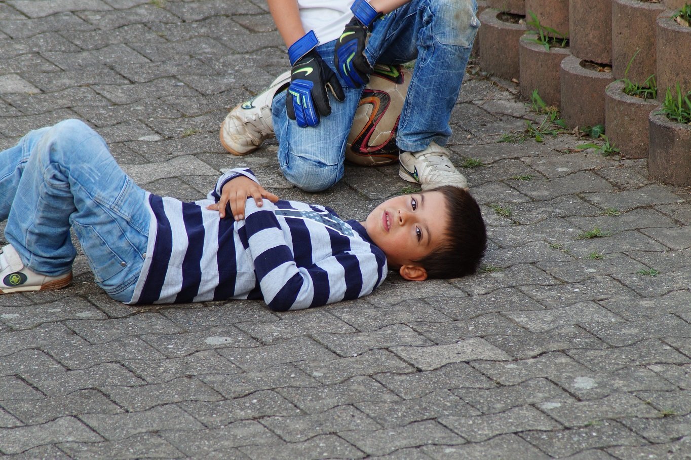 child lying on the street with soccer ball