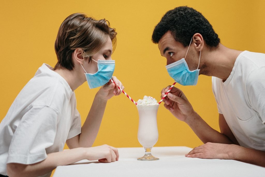 Two people sharing a milkshake while wearing masks